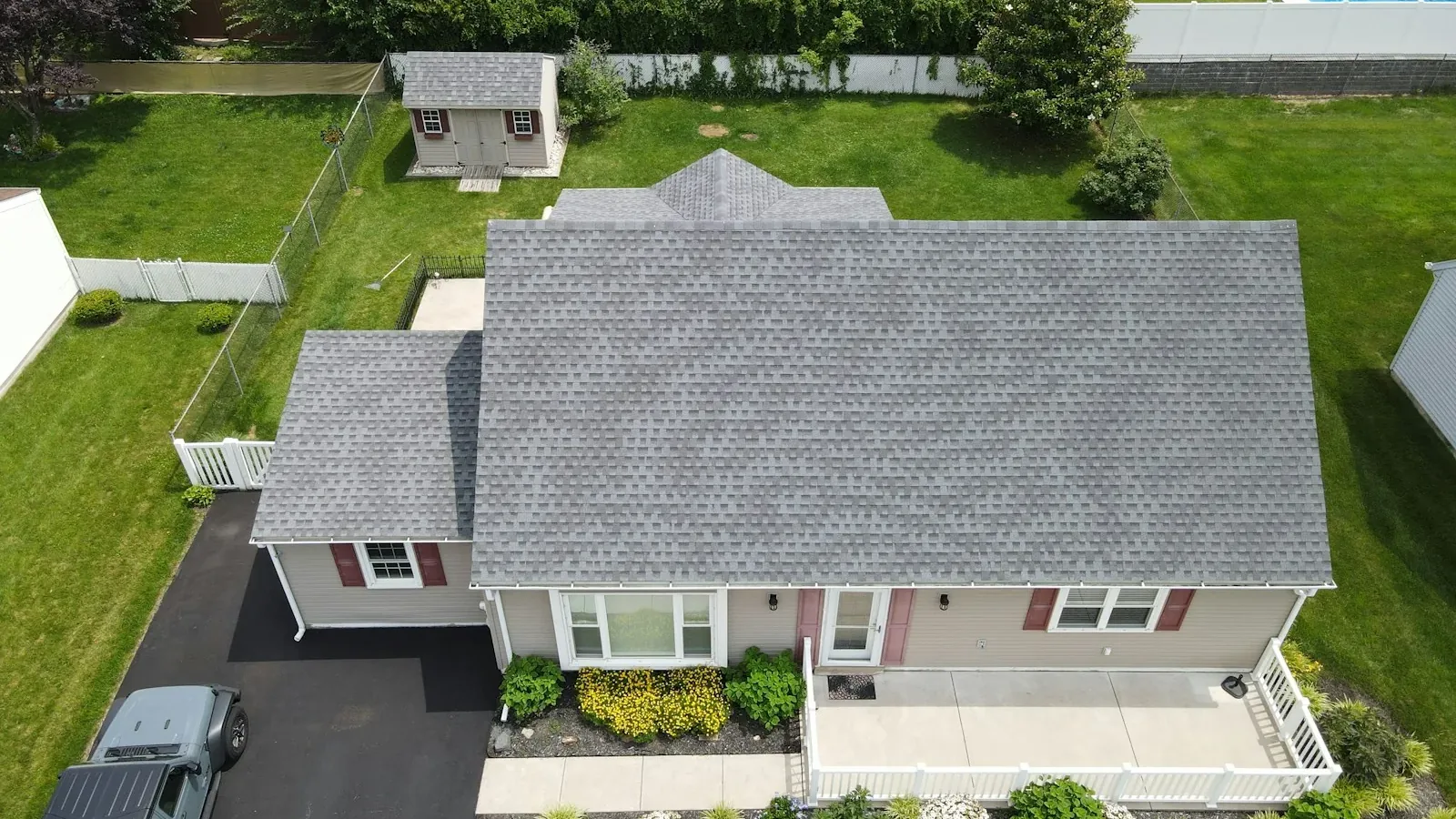 Aerial view of a suburban house with a grey asphalt shingle roof and mown lawn