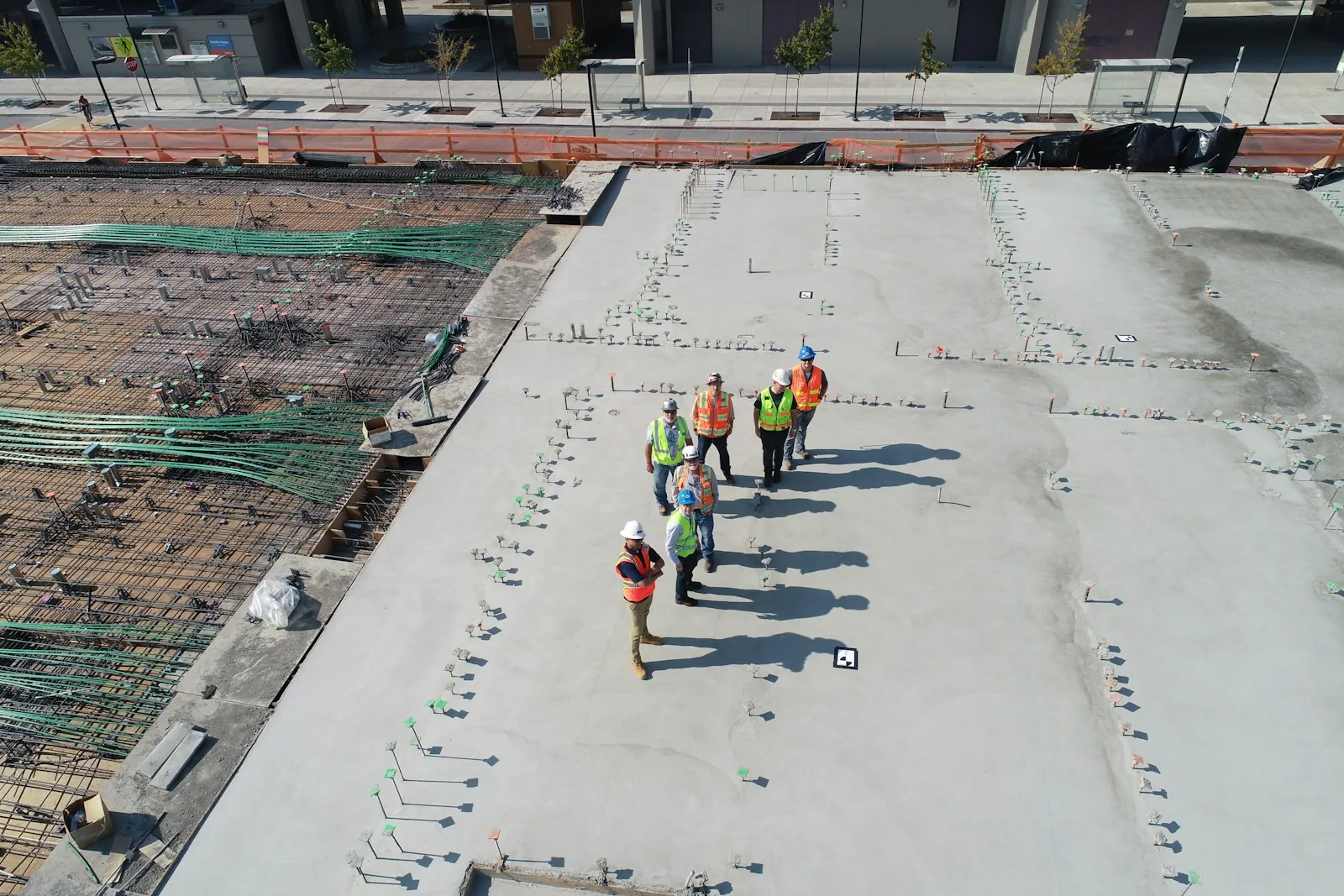 A small crew of construction workers standing together on a freshly poured concrete deck beside rebar