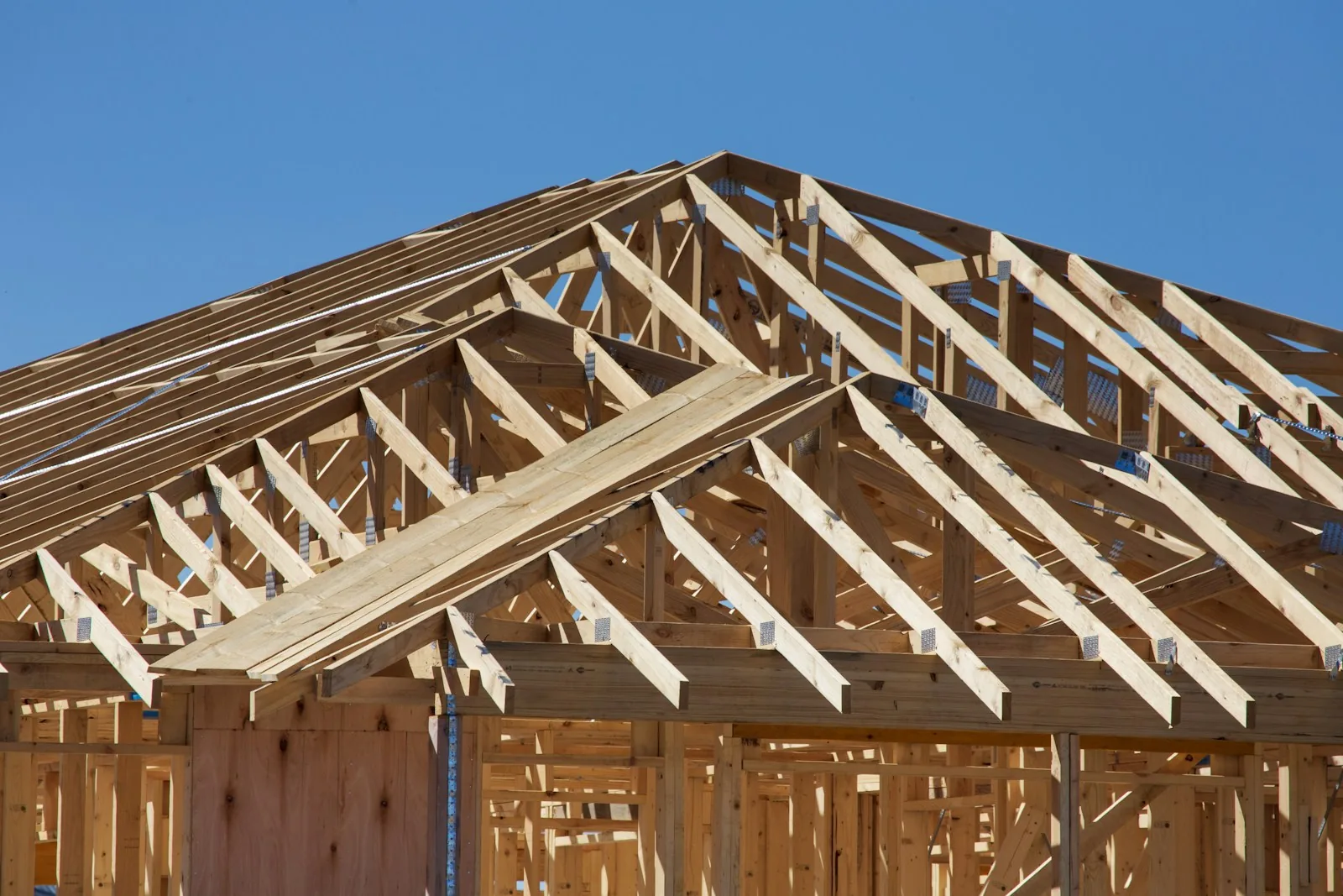 A house under construction with exposed wooden roof framing against a clear sky