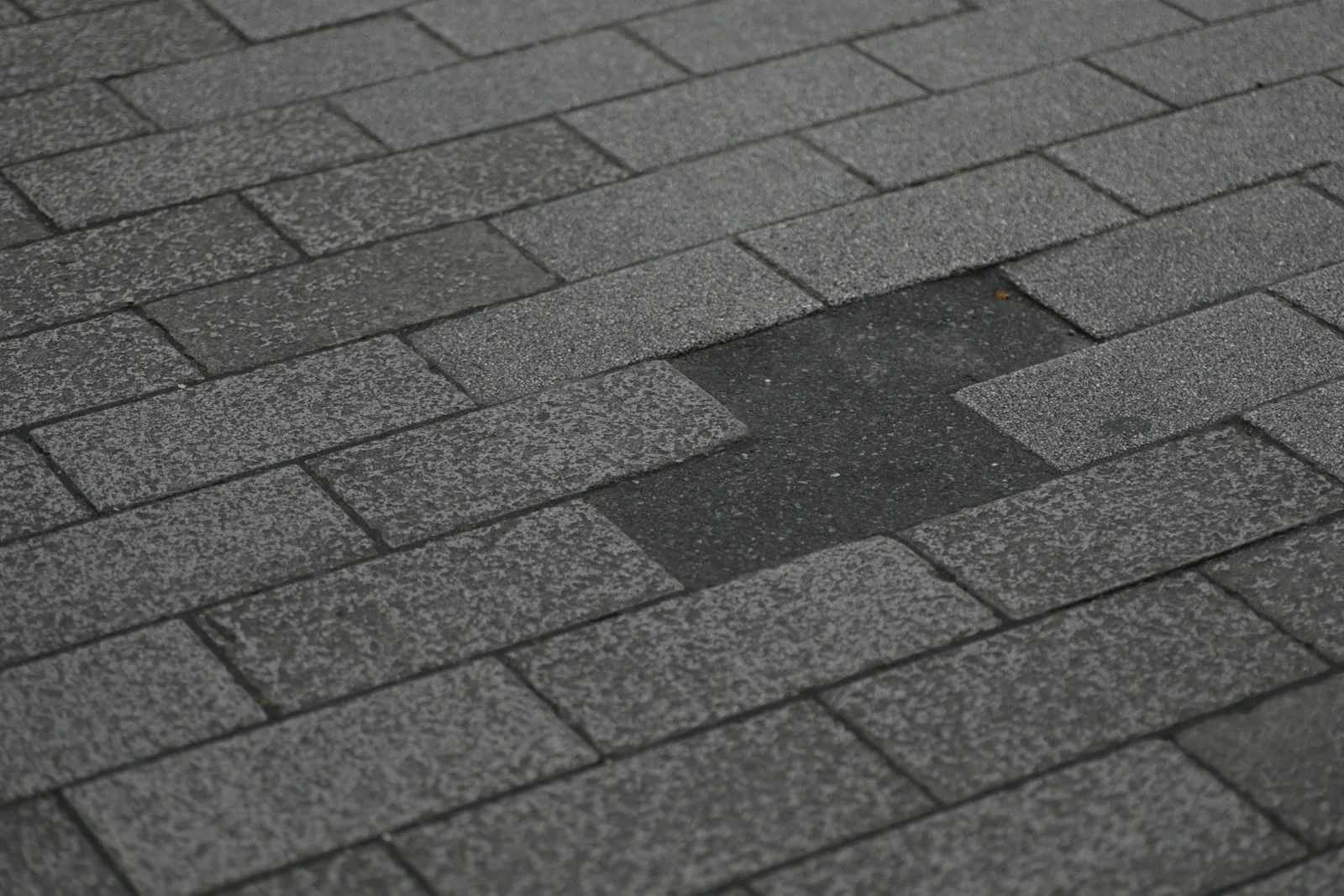 Close up of gray asphalt roof shingles with one shingle missing exposing the layer beneath