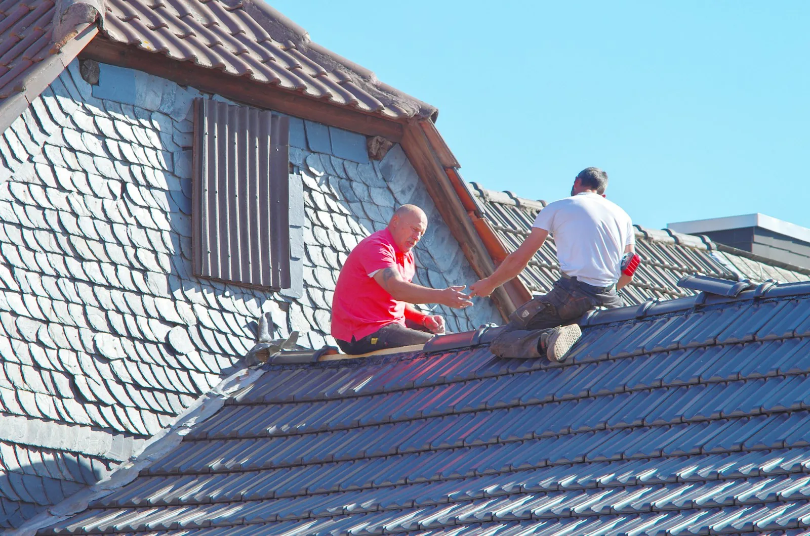 Two roofing contractors working on a residential roof on a clear day