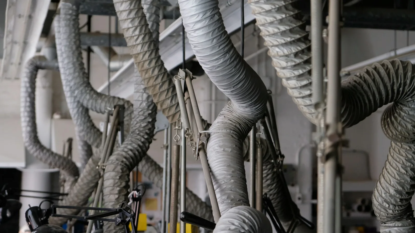 Flexible grey ventilation ducts running along the ceiling of an industrial workspace